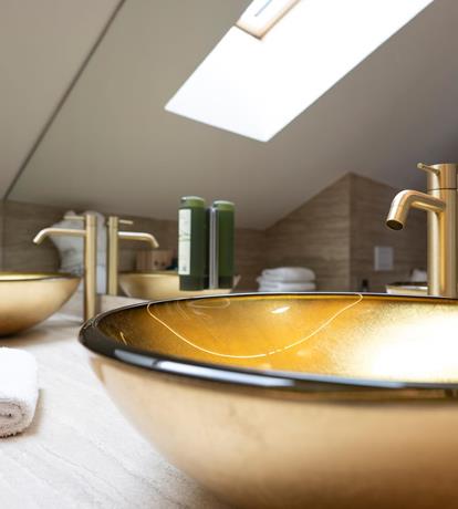 Bagno mansardato di design con lavabo in appoggio dorato e lucernario sul tetto