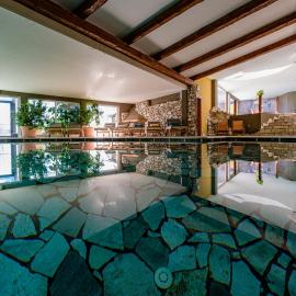 SPA -piscina riscaldata interna in stile alpino con pietra naturale, travi in legno e zona lettini, ideale per rilassarsi dopo una giornata sugli sci o trekking sull’Altopiano della Paganella