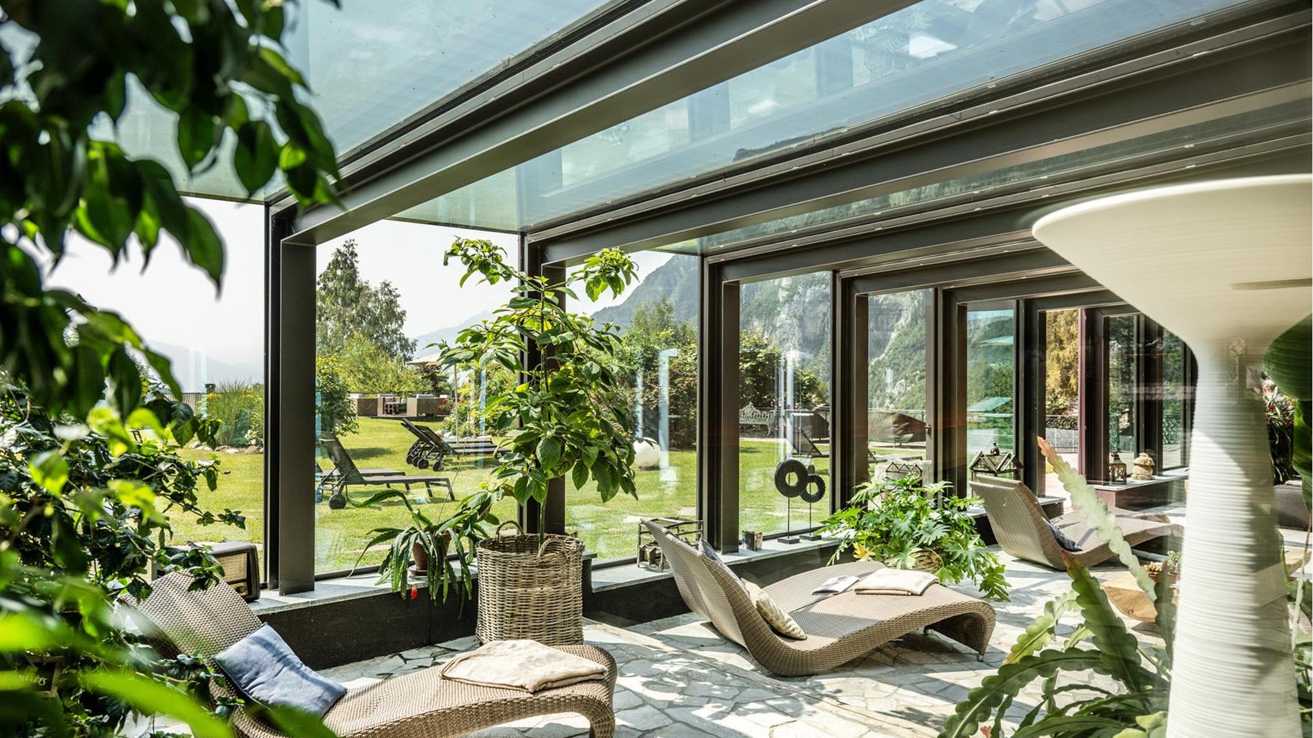 Luminoso spazio relax con ampie vetrate panoramiche allo Sport Hotel Panorama di Fai della Paganella. Comode chaise longue, luce naturale e vista sul giardino e sulle montagne del Trentino creano un’atmosfera rigenerante