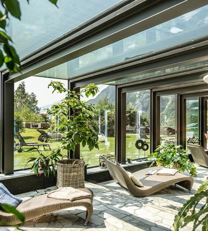 Luminoso spazio relax con ampie vetrate panoramiche allo Sport Hotel Panorama di Fai della Paganella. Comode chaise longue, luce naturale e vista sul giardino e sulle montagne del Trentino creano un’atmosfera rigenerante