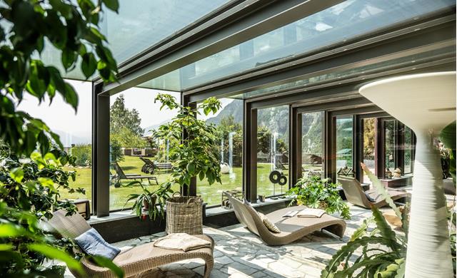 Luminoso spazio relax con ampie vetrate panoramiche allo Sport Hotel Panorama di Fai della Paganella. Comode chaise longue, luce naturale e vista sul giardino e sulle montagne del Trentino creano un’atmosfera rigenerante